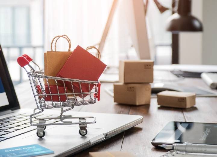 A small shopping cart and parcels on a desk beside a laptop
