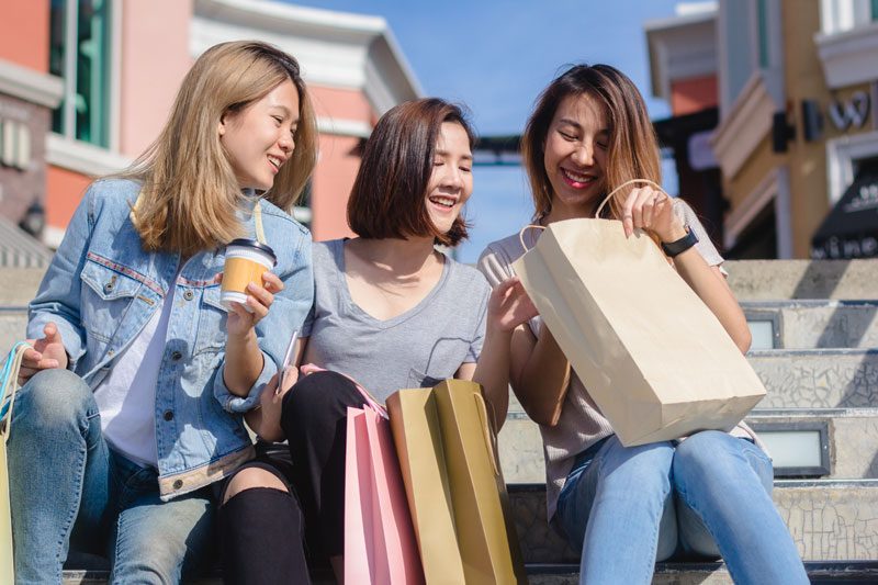 Three friends sitting on steps with their shopping bags